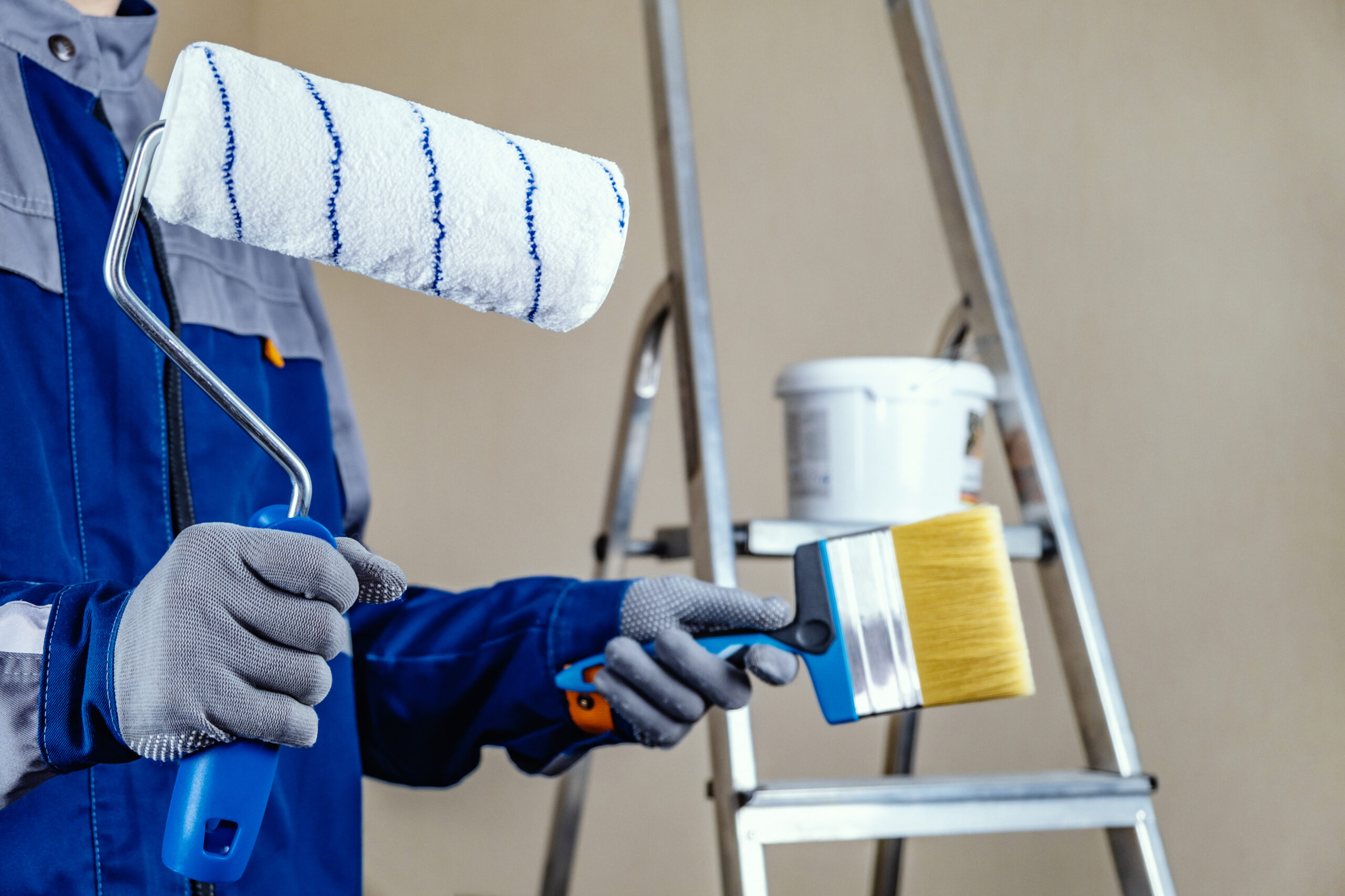 The plaster painter is ready to paint the wall. In the hands of a roller and brush. A stepladder and a bucket of paint in the background